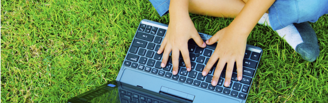 child typing on laptop keyboard