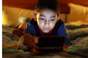 Young boy playing handheld video game device while lying on his bed