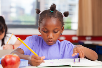 Young child writing in a notebook in a school setting