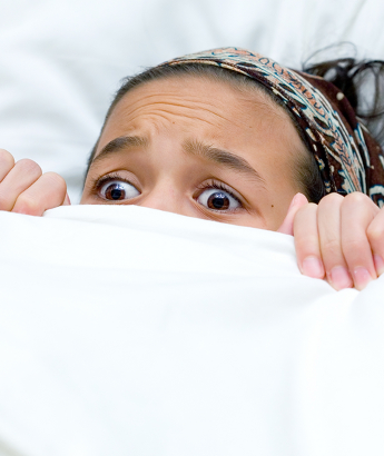 girl looking scared and hiding under the covers