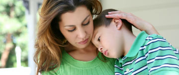 A mother holding and soothing her son who looks sad and/or sick