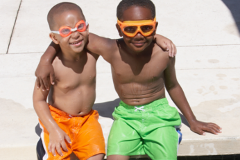 Two young boys wearing swimming goggles and sitting at the edge of a pool