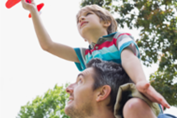 Boy sitting on his father's shoulders playing with a toy plane